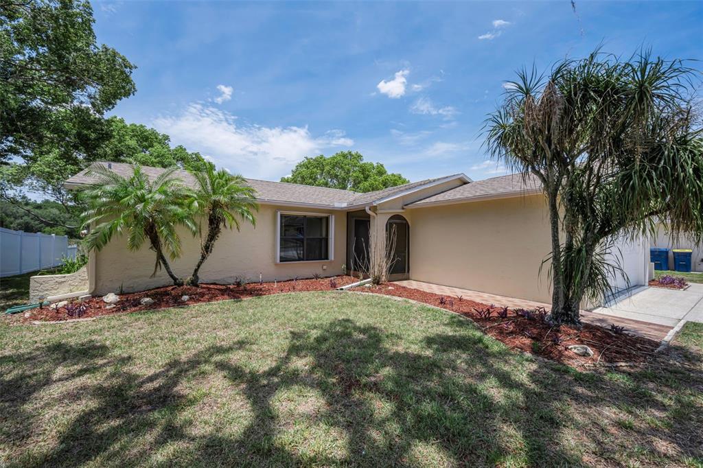 A single-story house with a beige stucco exterior, palm trees, and a landscaped front yard — 12603 PECAN TREE DRIVE, HUDSON, FL