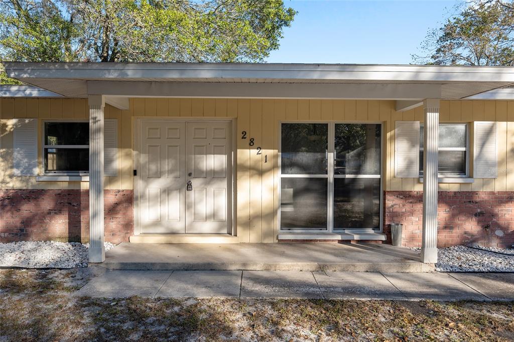 The exterior of a single-story house features a brick base, yellow siding, and double doors — 2821 NE 17TH TER, GAINESVILLE, FL
