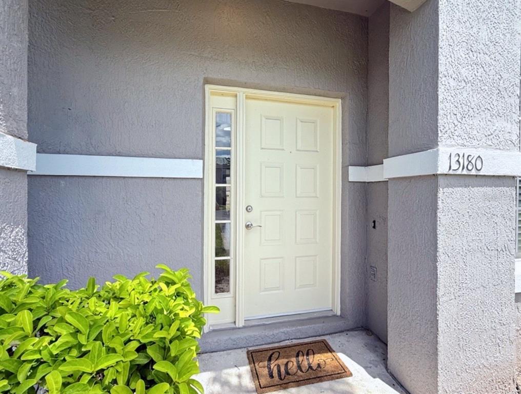 A light-colored front door with a side window sits under a covered entryway — 13180 SUMMERTON DRIVE, ORLANDO, FL
