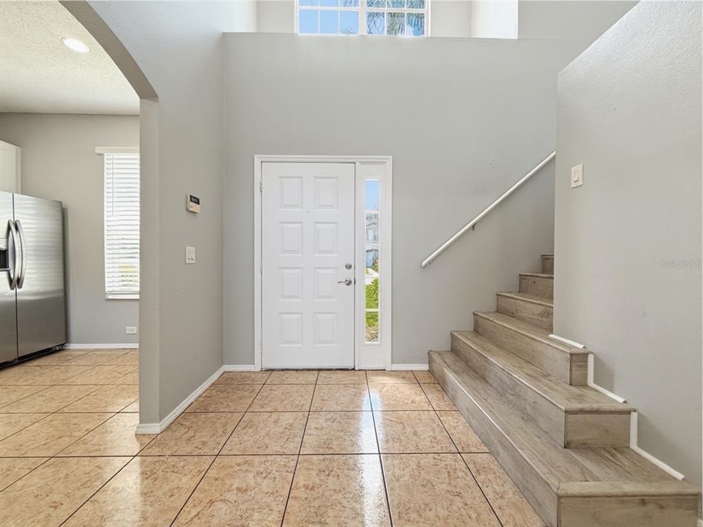 An entryway features tiled flooring, a white front door, and a staircase with wood-look steps — 13180 SUMMERTON DRIVE, ORLANDO, FL