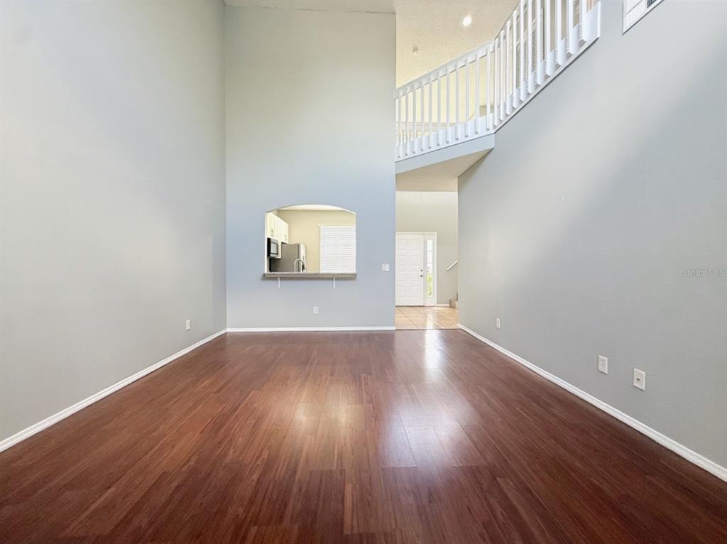 An empty living room with high ceilings, wood-look flooring, and a pass-through to the kitchen — 13180 SUMMERTON DRIVE, ORLANDO, FL
