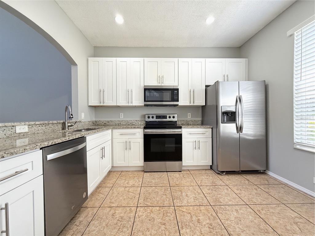 A kitchen features white cabinets, granite countertops, stainless steel appliances, and tan tile flooring — 13180 SUMMERTON DRIVE, ORLANDO, FL