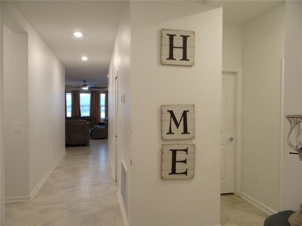 A hallway with light tile flooring leads to a living area with wall-mounted decor — 6935 PERCH HAMMOCK LOOP, GROVELAND, FL