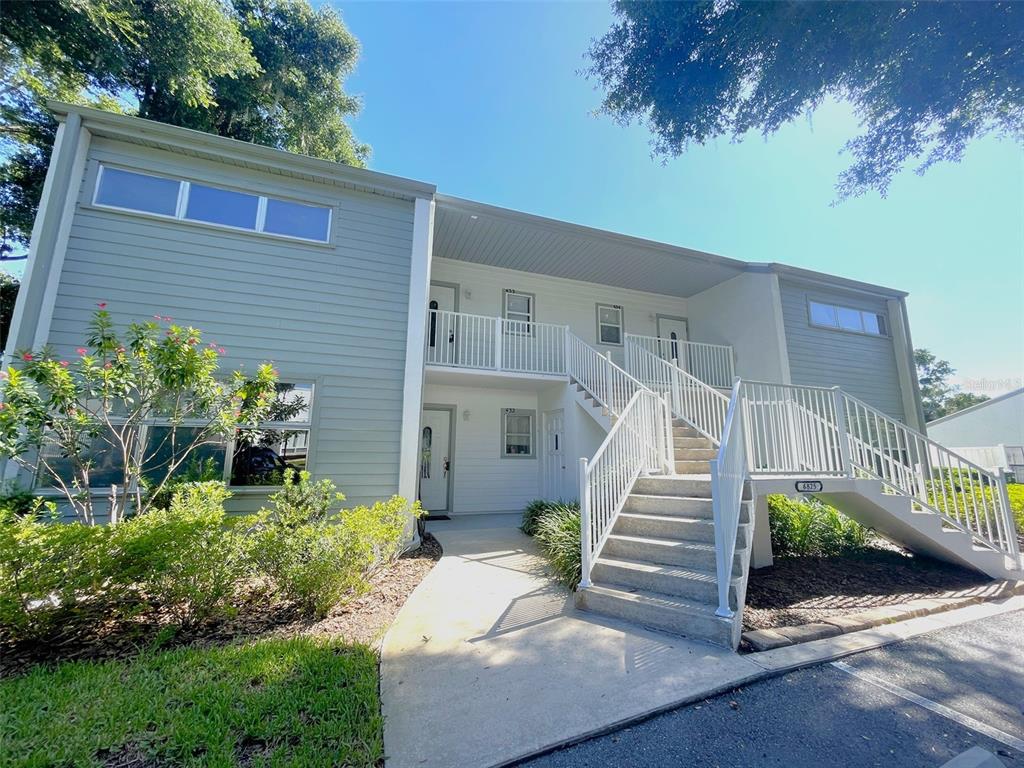 A two-story apartment building exterior features light gray siding, a concrete staircase, and white railings — 6825 E DOWNING STREET UNIT 432, INVERNESS, FL