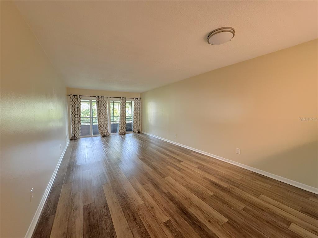 An empty living room features wood-look flooring, light-colored walls, and sliding glass doors with curtains — 6825 E DOWNING STREET UNIT 432, INVERNESS, FL