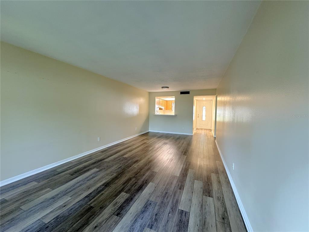 An empty living room features light-colored walls, wood-look laminate flooring, and a kitchen pass-through window — 6825 E DOWNING STREET UNIT 432, INVERNESS, FL