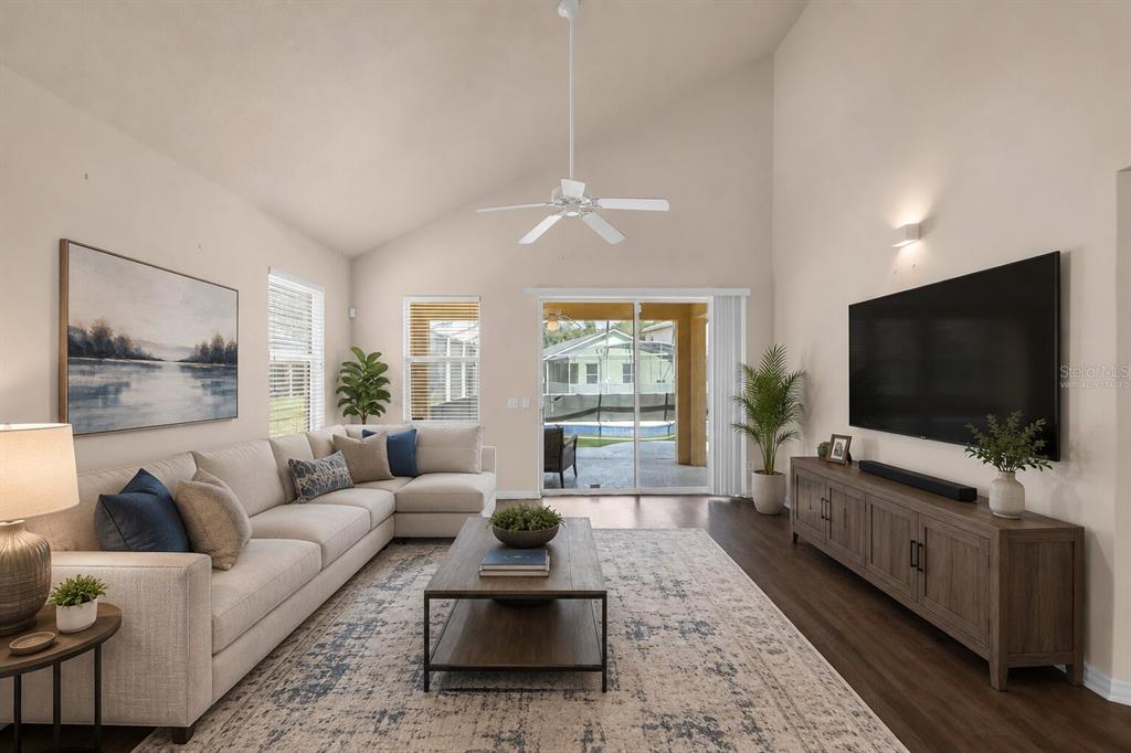 A living room with a vaulted ceiling, sectional sofa, television, and sliding glass patio doors — 1755 ROYAL RIDGE DRIVE, DAVENPORT, FL