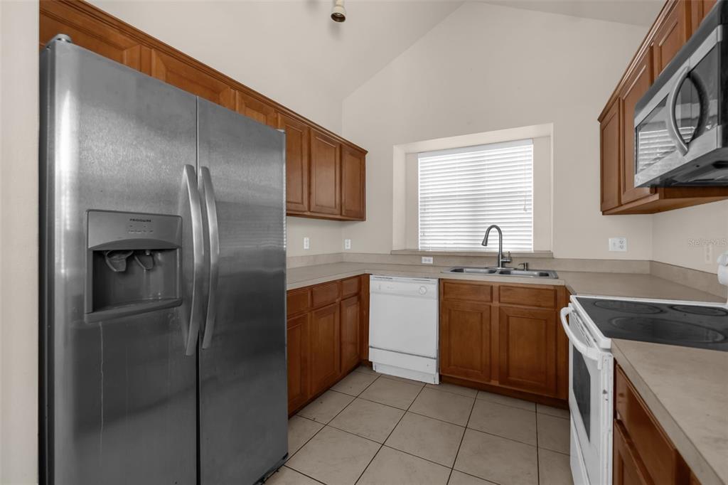 A kitchen with wooden cabinets, stainless steel refrigerator, white appliances, and tiled flooring — 1755 ROYAL RIDGE DRIVE, DAVENPORT, FL