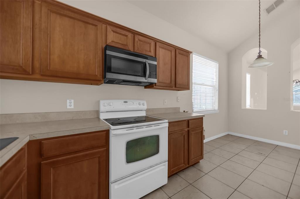 A kitchen features wood cabinets, a white stove, a microwave, and tile flooring — 1755 ROYAL RIDGE DRIVE, DAVENPORT, FL