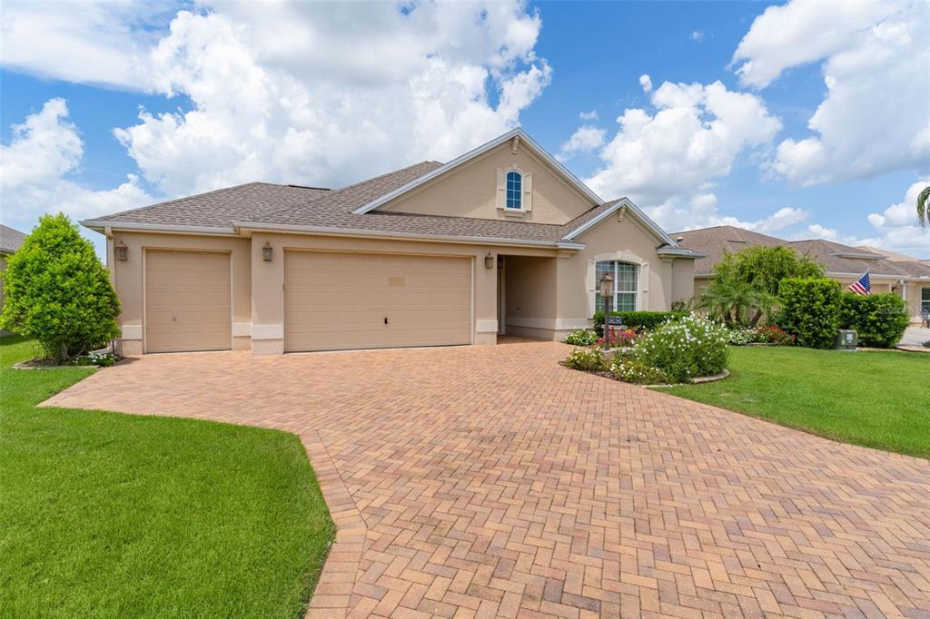 A single-story house with a beige stucco exterior, a brick paver driveway, and a garage — 3452 BOSIE RUN, THE VILLAGES, FL
