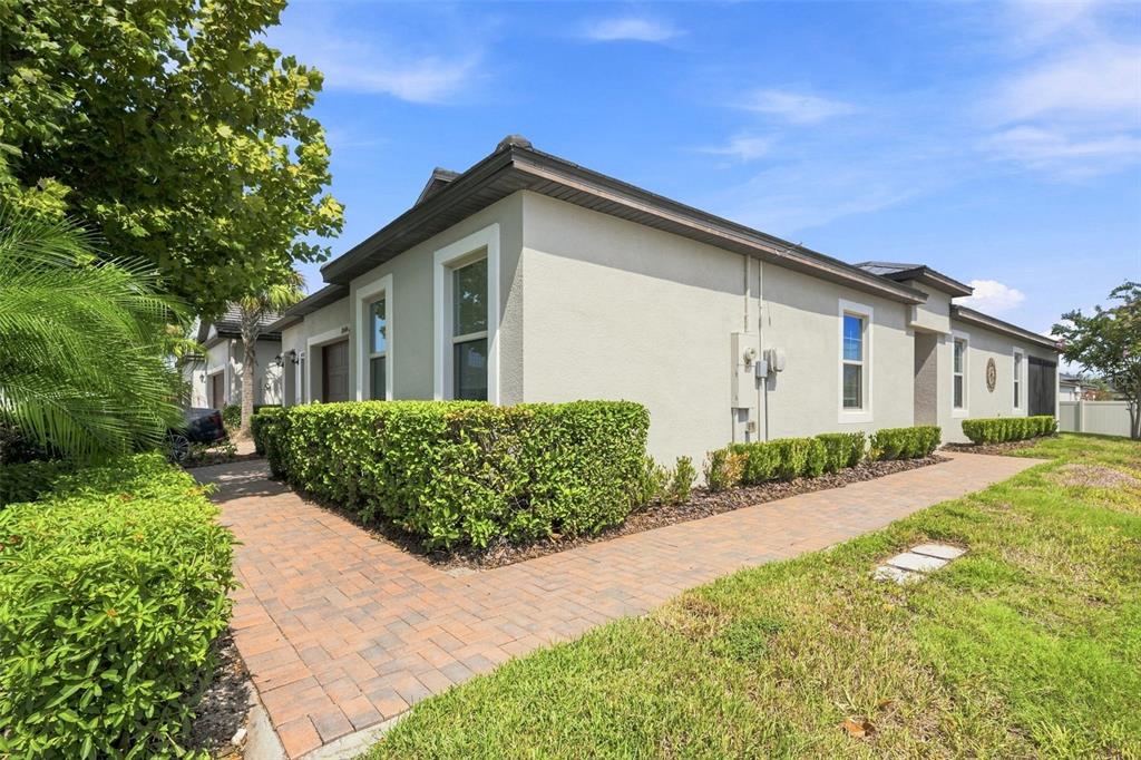 A side view of a beige house with a brick walkway and manicured hedges — 10444 WELDON CORK WAY, SAN ANTONIO, FL