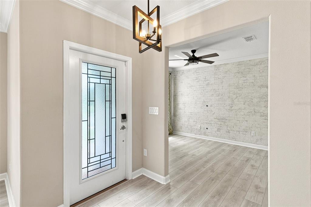 An entryway with a glass-paneled door, geometric chandelier, and an adjacent room with brick-patterned wallpaper — 10444 WELDON CORK WAY, SAN ANTONIO, FL