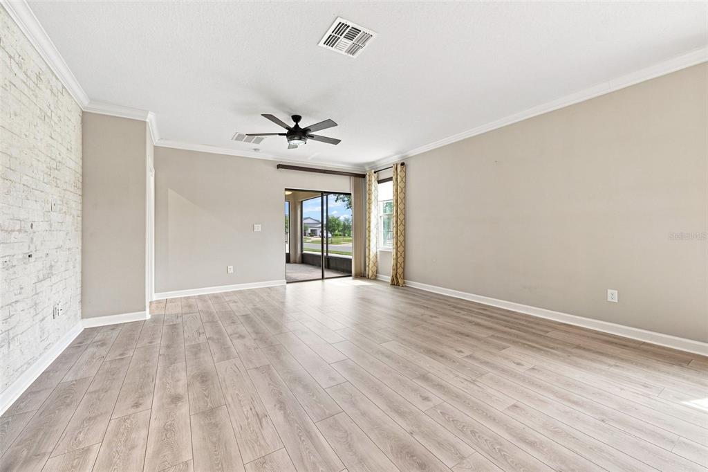 A living room with light wood-look flooring, a white brick accent wall, and sliding glass doors — 10444 WELDON CORK WAY, SAN ANTONIO, FL