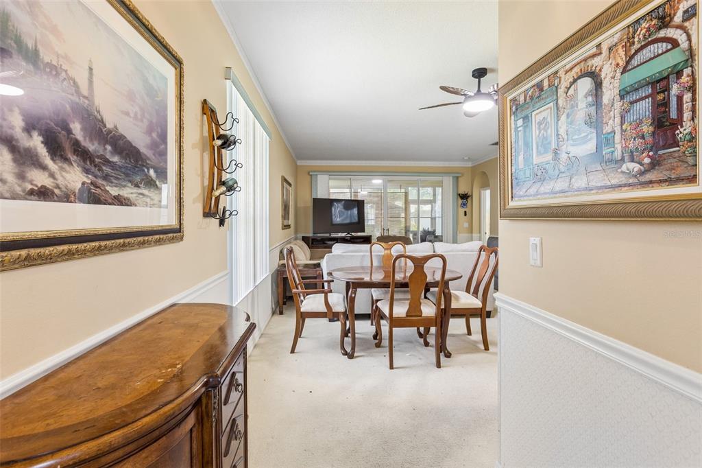 A dining area with a wooden table and chairs sits before a living room space — 4726 SAINT ANDREWS ARCADE, LEESBURG, FL