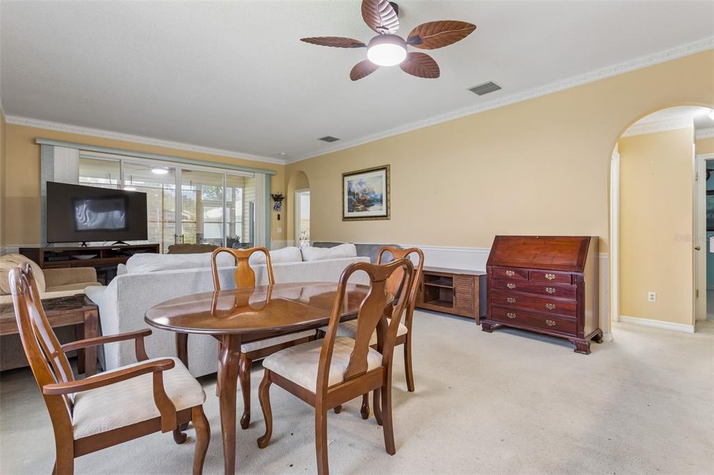 A dining area with a wooden table and chairs sits in front of a living room — 4726 SAINT ANDREWS ARCADE, LEESBURG, FL