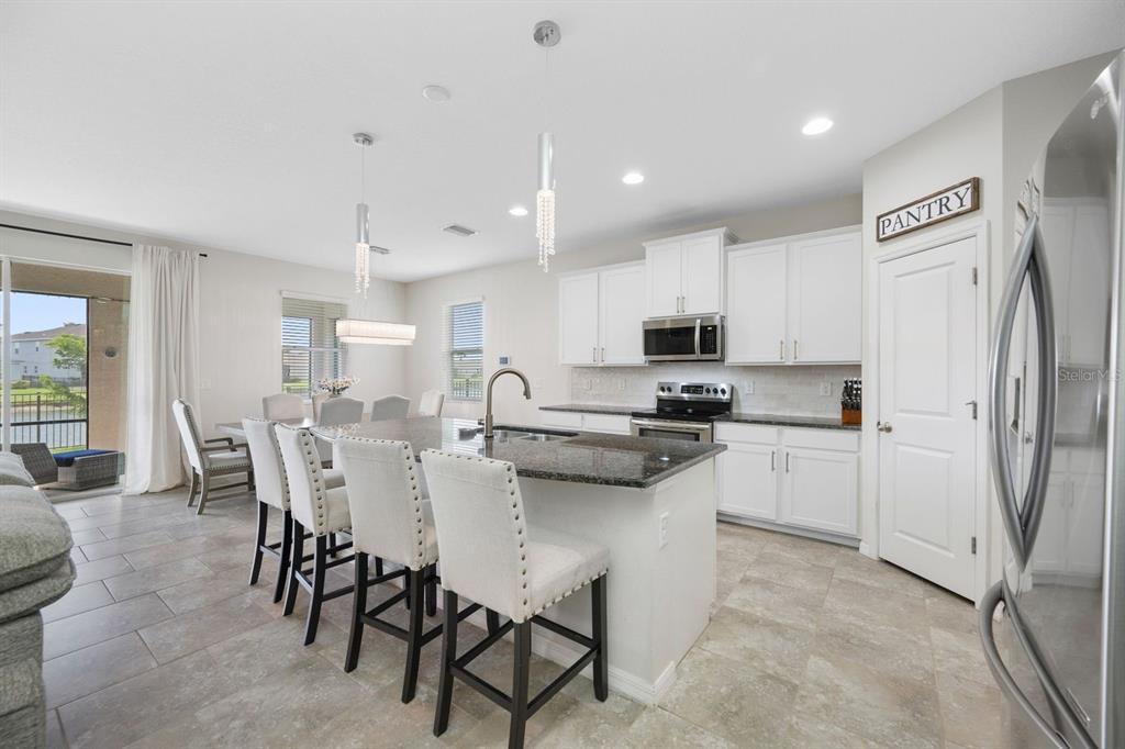 A kitchen with white cabinets, granite countertops, a center island with bar seating, and dining area — 6549 DEVESTA LOOP, PALMETTO, FL