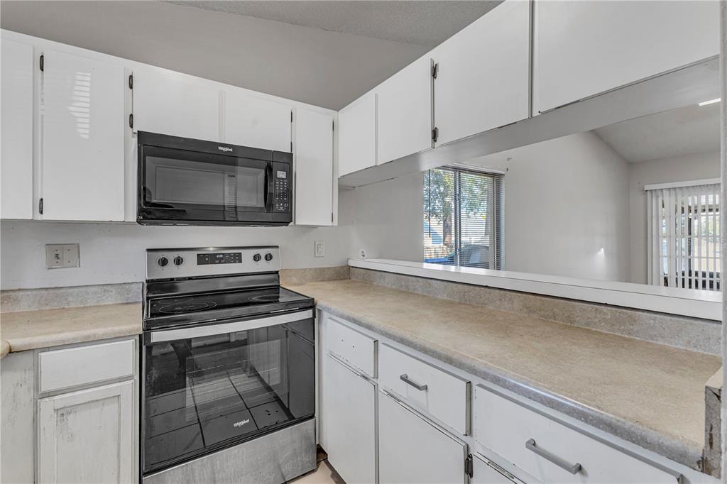 A kitchen with white cabinets, a black microwave and stove, and a pass-through window — 3675 WESTLAND COURT, ORLANDO, FL