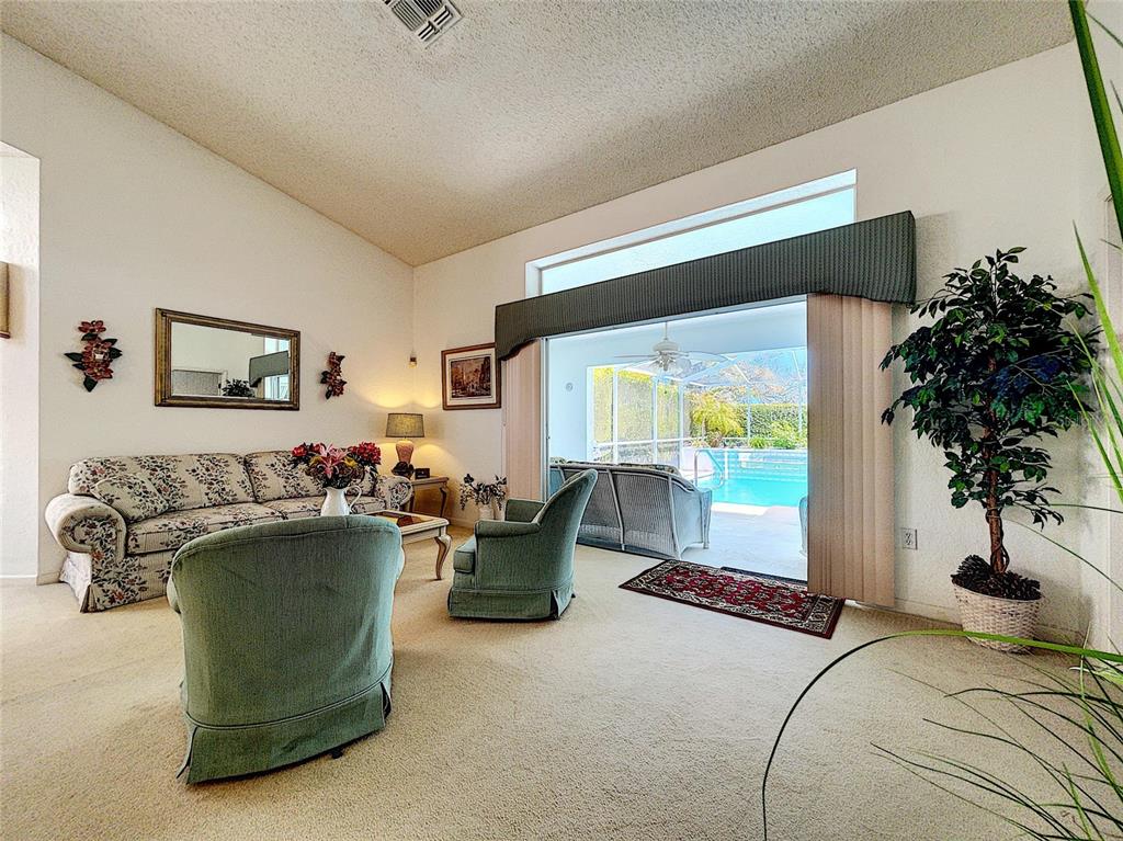 A living room with floral sofa, two green armchairs, and sliding doors opening to a pool — 9408 NEW ORLEANS DRIVE, WEEKI WACHEE, FL