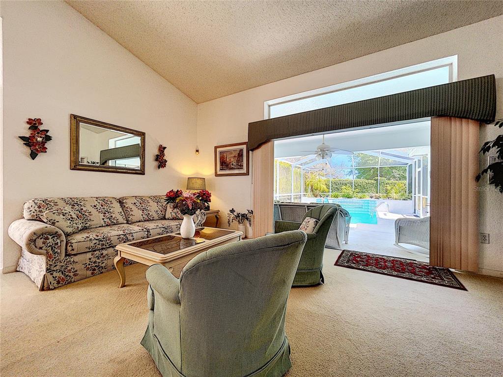 A living room with floral sofa, green armchairs, and a sliding door to a pool patio — 9408 NEW ORLEANS DRIVE, WEEKI WACHEE, FL