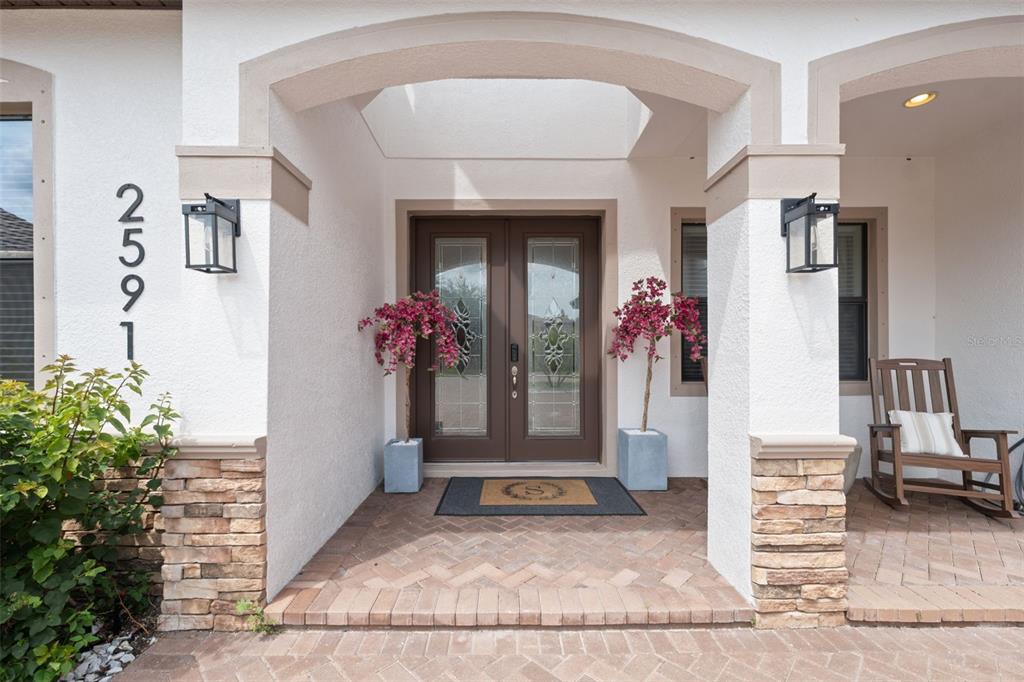 A covered entryway features a brick-paved porch, double front doors, and stone-accented columns — 2591 GRAND CYPRESS BOULEVARD, PALM HARBOR, FL