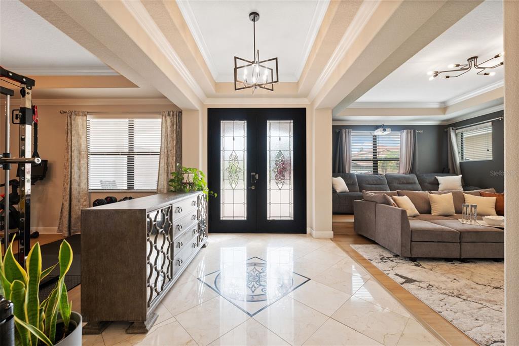 A foyer with tile flooring and a central medallion leads to a living room and gym — 2591 GRAND CYPRESS BOULEVARD, PALM HARBOR, FL