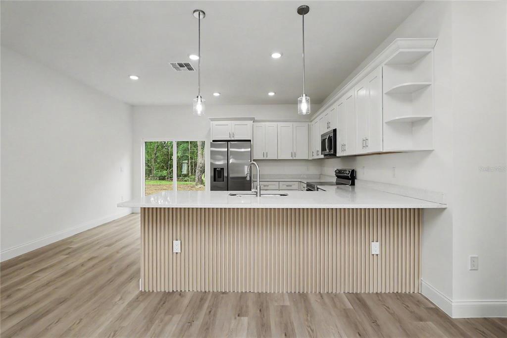 A modern kitchen features white cabinetry, stainless steel appliances, and light wood-look flooring — 16503 SW 31ST TERRACE, OCALA, FL