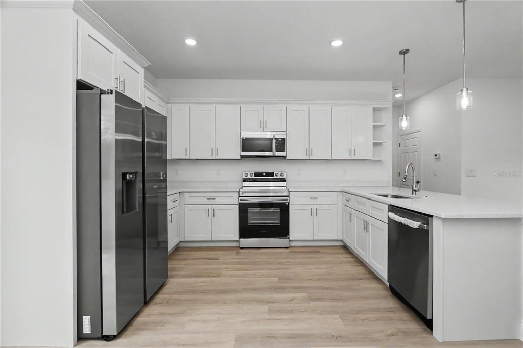 A modern kitchen features white cabinetry, a quartz island with a sink, and stainless appliances — 16503 SW 31ST TERRACE, OCALA, FL