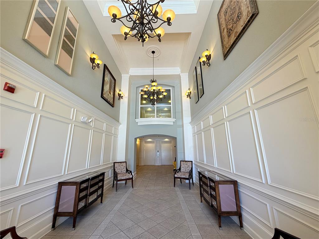 A formal entryway features high ceilings, two chandeliers, wainscoting, and symmetrical furniture with chairs — 3368 ROBERT TRENT JONES DRIVE UNIT 10408, ORLANDO, FL