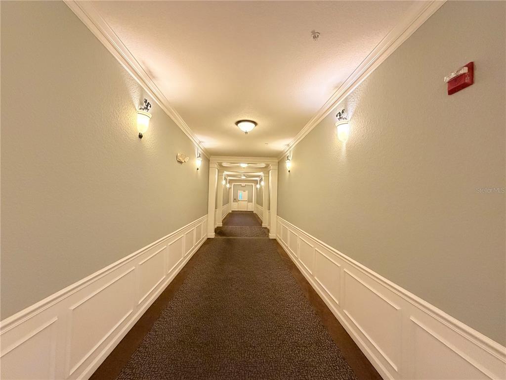 A long, carpeted indoor hallway features white wainscoting, wall sconces, and a recessed ceiling — 3368 ROBERT TRENT JONES DRIVE UNIT 10408, ORLANDO, FL