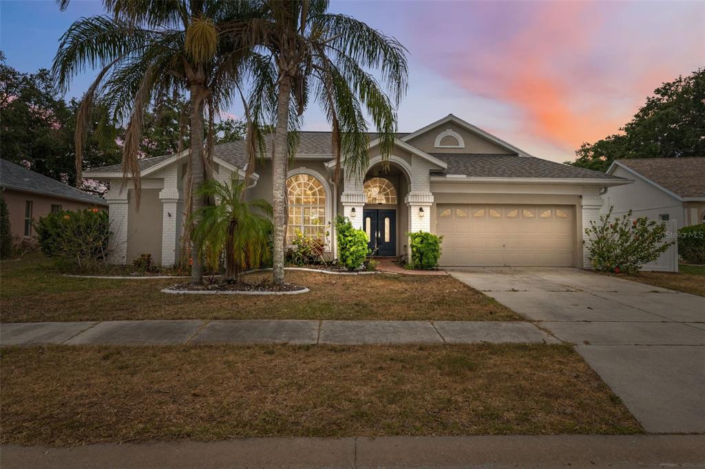 A single-story suburban house with a two-car garage, palm trees, and a brick-accented entryway — 9104 WATER HAZARD DRIVE, HUDSON, FL