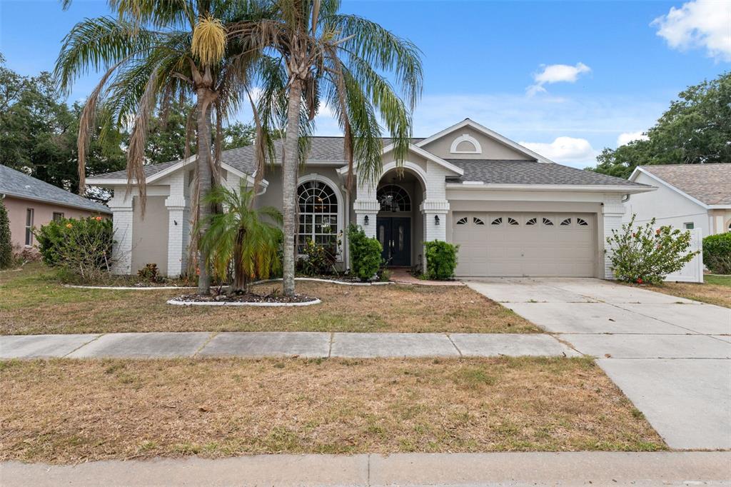 A single-story house with a beige stucco exterior, a two-car garage, and two palm trees — 9104 WATER HAZARD DRIVE, HUDSON, FL