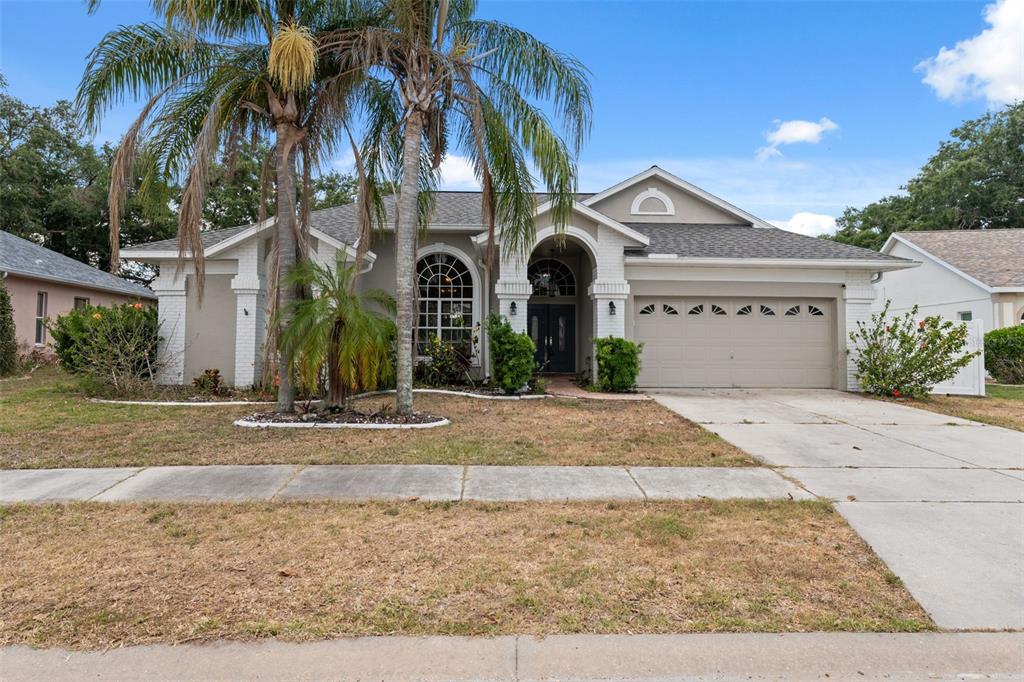 A single-story house with a beige stucco exterior, a two-car garage, and palm trees — 9104 WATER HAZARD DRIVE, HUDSON, FL