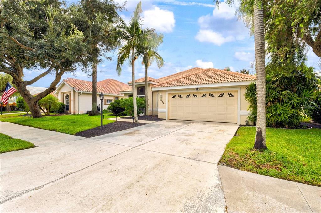 The exterior of a beige house features a landscaped garden, palm trees, and a walkway — 6252 DONNINGTON COURT, SARASOTA, FL
