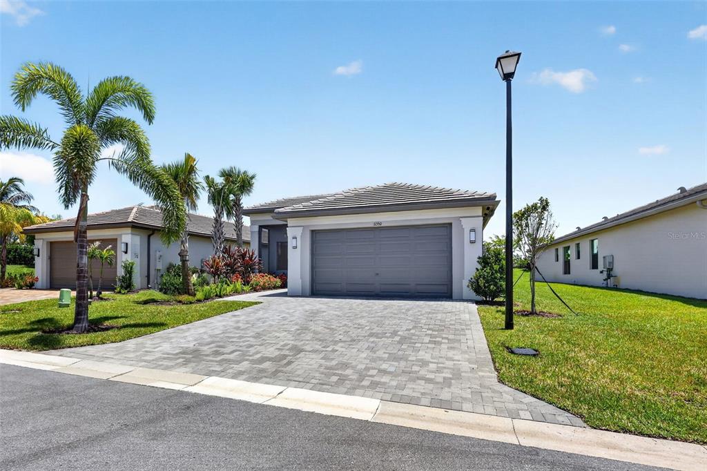 A single-story house with a gray garage, paver driveway, and palm trees under a blue sky — 11550 SW OCEANFRONT COURT, PORT ST LUCIE, FL