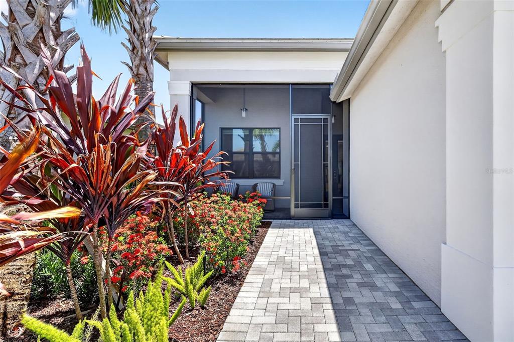 A paved walkway leads to a screened-in porch with red plants in the foreground — 11550 SW OCEANFRONT COURT, PORT ST LUCIE, FL