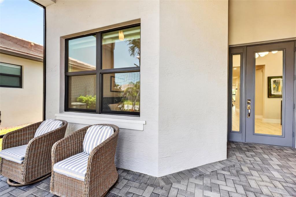 A covered patio with two wicker chairs sits beside a window and a glass-paneled front door — 11550 SW OCEANFRONT COURT, PORT ST LUCIE, FL