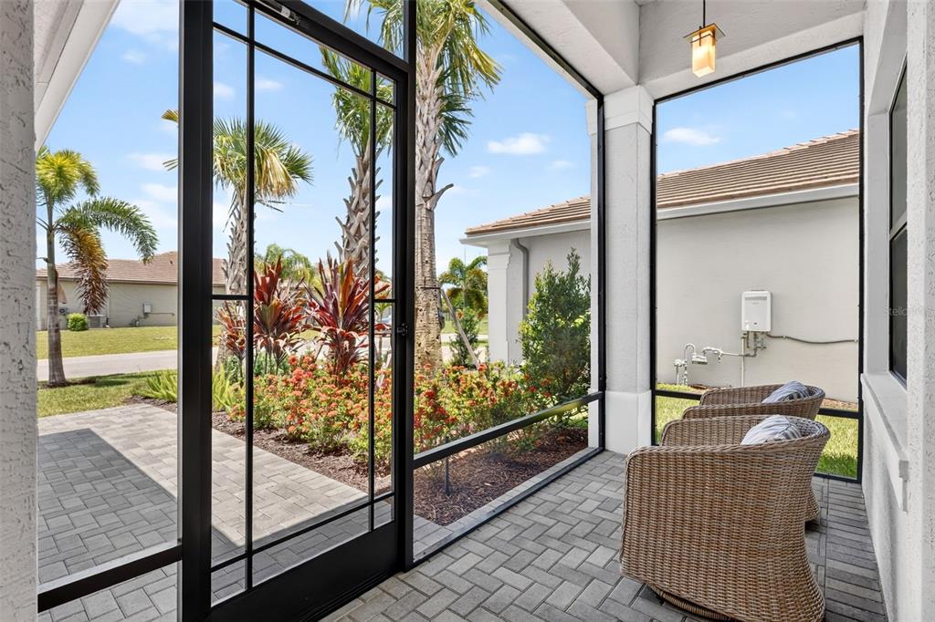 A screened-in patio features gray paver flooring, wicker chairs, and a view of landscaped gardens — 11550 SW OCEANFRONT COURT, PORT ST LUCIE, FL