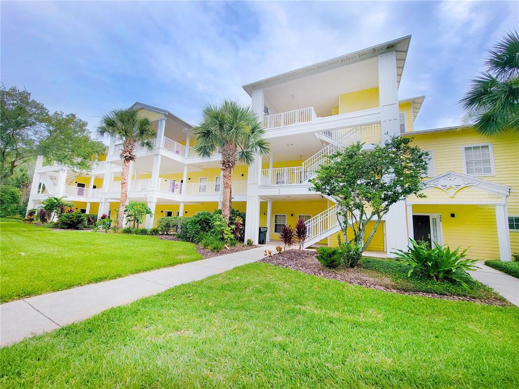 A three-story yellow apartment building features white railings, exterior staircases, and palm trees — 716 LUCAYA LOOP UNIT B1/U716, DAVENPORT, FL