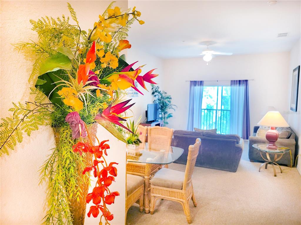 A bright living and dining area features wicker furniture, a glass table, and floral decor — 716 LUCAYA LOOP UNIT B1/U716, DAVENPORT, FL