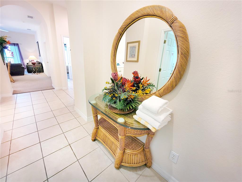 A hallway features a wicker console table with a glass top, mirror, and floral arrangement — 716 LUCAYA LOOP UNIT B1/U716, DAVENPORT, FL