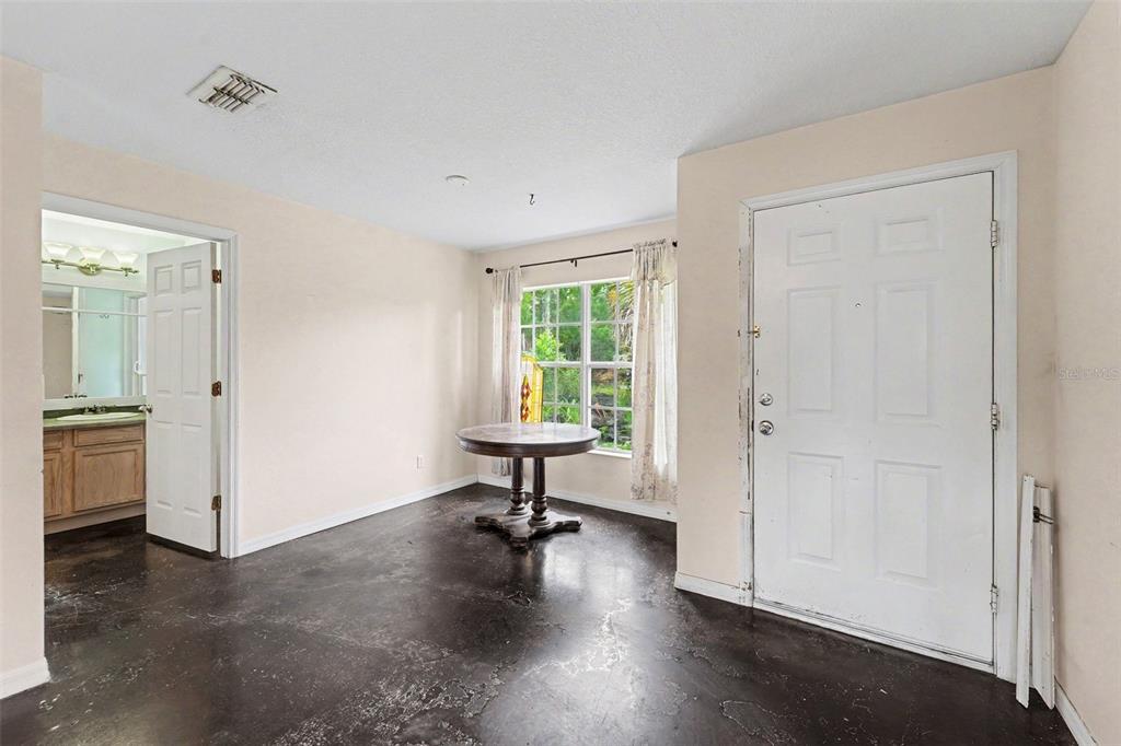 A room with dark concrete flooring, a round table, a window, and an adjacent bathroom — 7295 CENTERWOOD AVENUE, SPRING HILL, FL