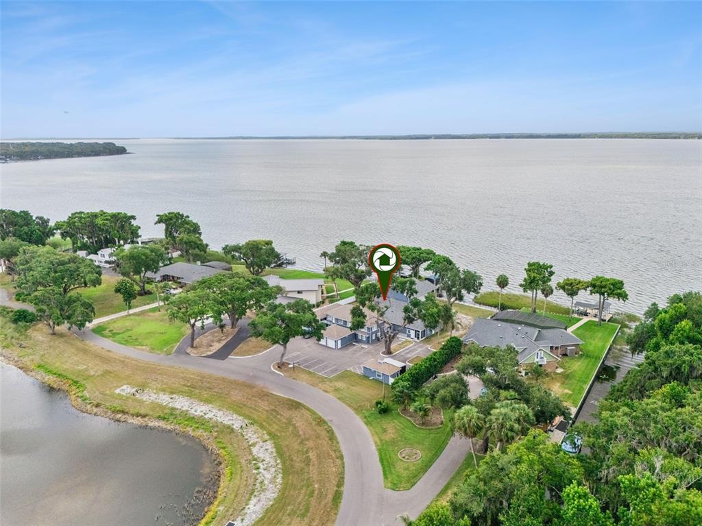 An aerial view shows a multi-unit building complex situated on a grassy waterfront property — 1023 MELLATHON CIRCLE, LEESBURG, FL