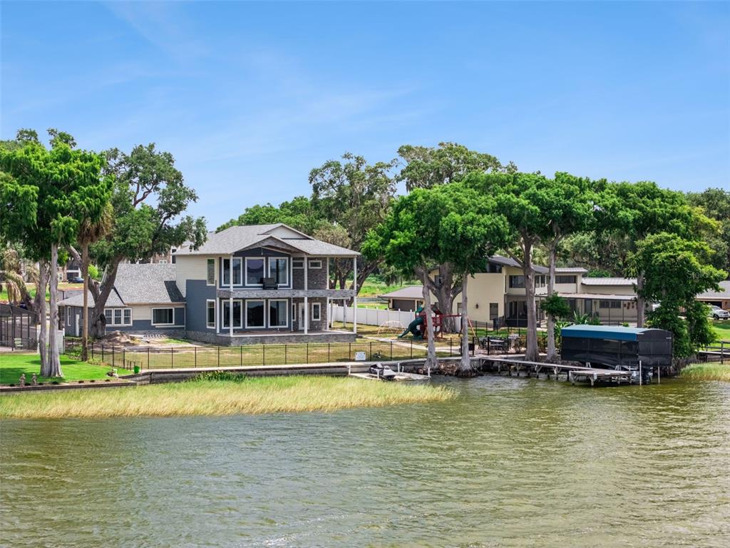 A two-story house with a stone facade sits on a grassy lot by a lake — 1023 MELLATHON CIRCLE, LEESBURG, FL