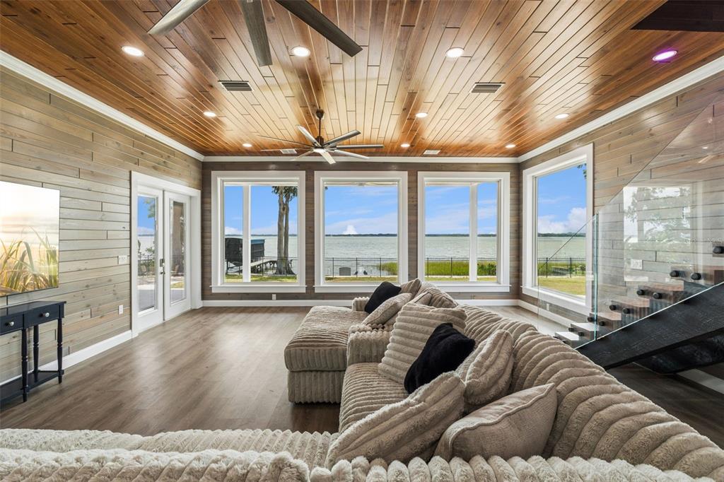 A living room with wood-paneled walls and ceiling, a large sectional sofa, and lake views — 1023 MELLATHON CIRCLE, LEESBURG, FL