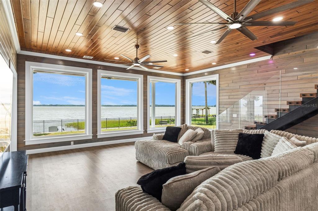 A living room with wood-paneled walls and ceilings, large windows, and views of a lake — 1023 MELLATHON CIRCLE, LEESBURG, FL