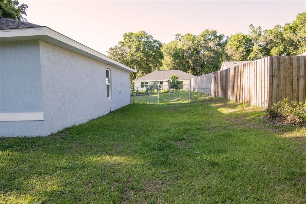 A side yard features a light blue house exterior, a wooden fence, and green grass — 3661 SE 131ST PLACE, BELLEVIEW, FL