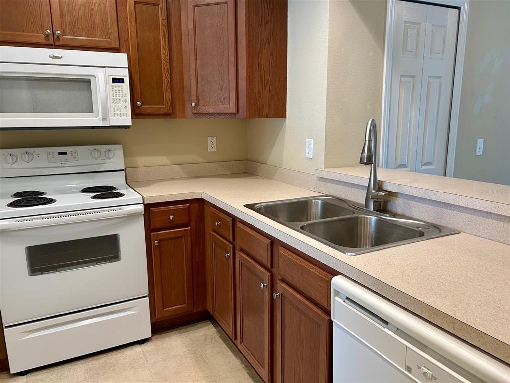 A kitchen features wood cabinets, white appliances, a double-basin sink, and beige laminate countertops — 2078 SUN DOWN DRIVE, CLEARWATER, FL