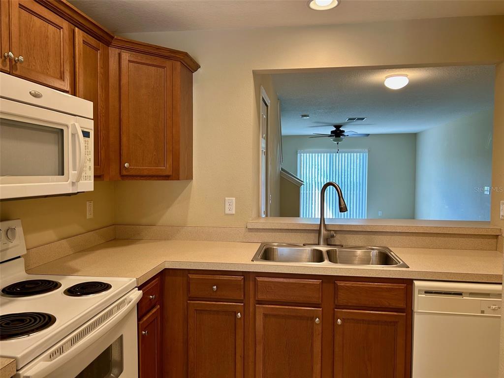 A kitchen features wood cabinets, beige countertops, a double sink, and a white appliance suite — 2078 SUN DOWN DRIVE, CLEARWATER, FL