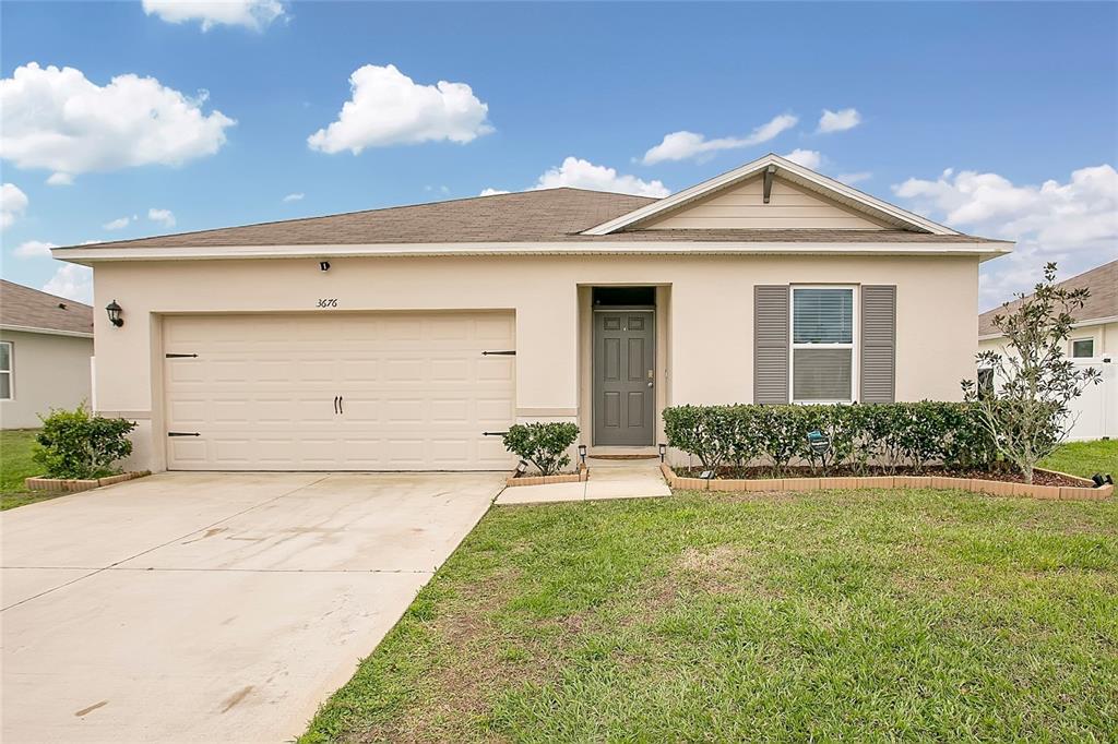 A single-story house features a beige stucco exterior, a two-car garage, and a front lawn — 3676 SCARLET OAK DRIVE, ST CLOUD, FL