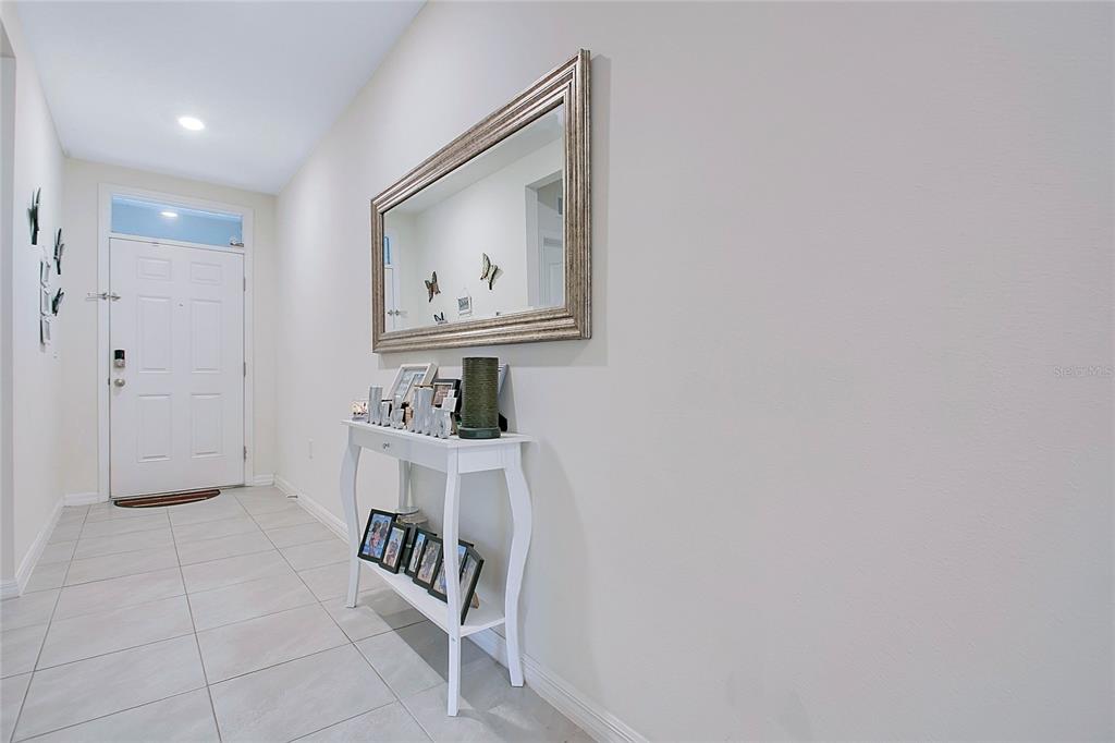 A white entryway features a console table, a large wall mirror, and tiled flooring — 3676 SCARLET OAK DRIVE, ST CLOUD, FL